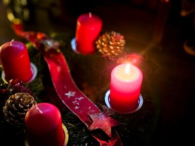 Rote Adventskerzen mit Deko, eine Kerze brennt im warmen Licht.