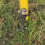 Gefundener Stoffhund in Ober-Ramstadt, schmutzig und nass, angelehnt an einen gelben Pfosten im hohen Gras am Feldrand. Rundherum liegen Blätter und trockenes Gras.