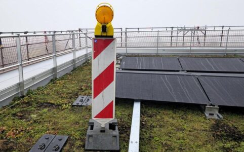 Eine einsame Baustellen-Warnbake steht auf einem Dach zwischen Solarmodulen und Nebel, als hätte sie sich dorthin verirrt 😁