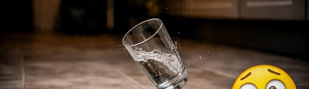 Eine Hand lässt ein Wasserglas über dunklen Fliesen fallen, daneben ein panischer Smiley, der Moment kurz vor dem Aufprall. KI generiert.