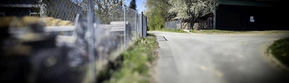 Straße am Hang, in der Ferne wirkt ein Schatten wie ein umgestürzter Zaun oder ein Tor