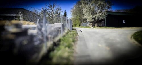 Straße am Hang, in der Ferne wirkt ein Schatten wie ein umgestürzter Zaun oder ein Tor