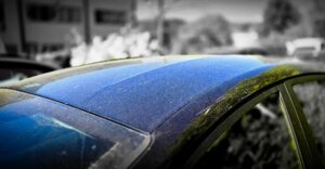 Gelbe Pollen und heller Staub auf dem schwarzen Autodach im Frühlingslicht.