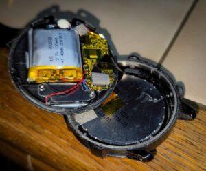 Geöffnete Smartwatch als unfreiwilliger Elektronikbausatz mit sichtbarem Akku, Platine und Kabeln.