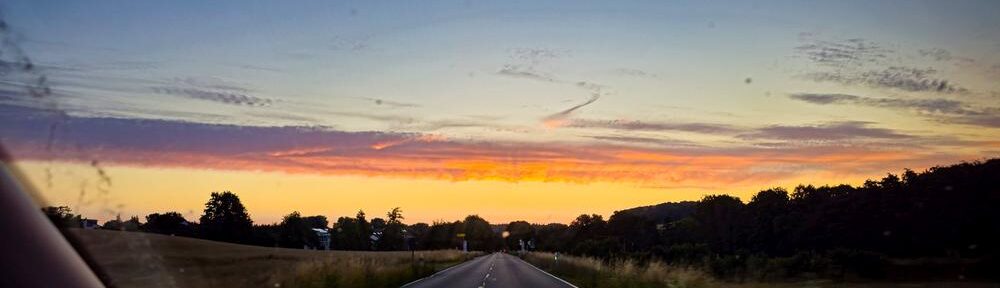 Morgenrot über der Straße auf dem ersten Arbeitsweg nach dem Urlaub, fotografiert durch die Windschutzscheibe.