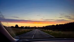Morgenrot über der Straße auf dem ersten Arbeitsweg nach dem Urlaub, fotografiert durch die Windschutzscheibe.