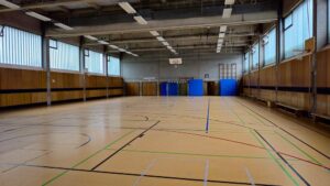 Leere Schulturnhalle mit Spielfeldlinien, Basketballkörben und blauen Matten.
