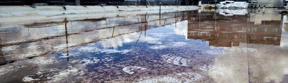 Spiegelungen und Fußspuren in einer großen Wasserfläche auf einem Flachdach in Hamburg.
