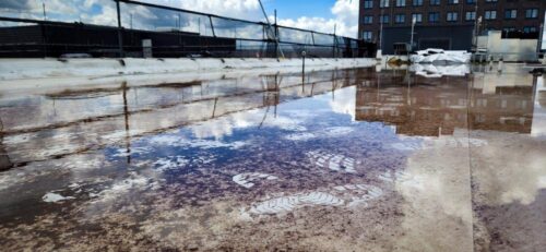 Spiegelungen und Fußspuren in einer großen Wasserfläche auf einem Flachdach in Hamburg.