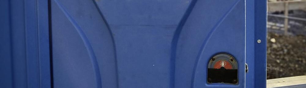 Blaue mobile Toilette auf einer Baustelle bei sommerlichem Wetter.