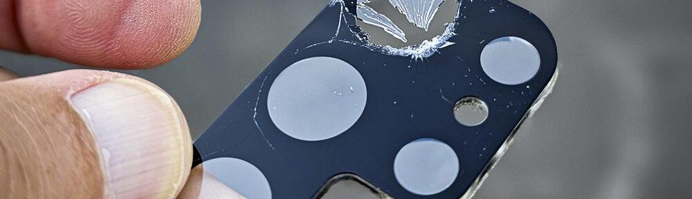 Beschädigte Schutzabdeckung der Smartphone-Kamera mit Loch und Rissen.
