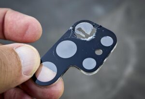 Beschädigte Schutzabdeckung der Smartphone-Kamera mit Loch und Rissen.